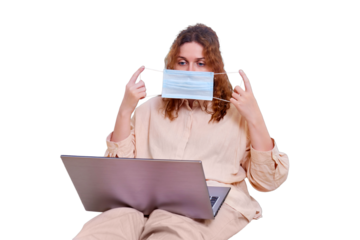 Cute woman takes off her medical mask while working from home, isolated on a white background. The woman is sitting at home with a laptop and a phone.