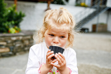 Cute toddler girl eating sweet birthday cupcake in an outdoor cafe. Happy child eats muffin.