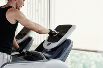 Mature man setting speed on treadmill when working out in gym