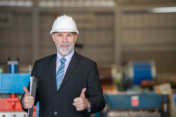 older owner engineer with beard mustache on face standing smile with his arms crossed at construction factory site. Boss manager in suit show good thumb at factory industry site.