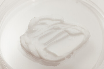 Fototapeta na wymiar White Face Moisturizing Cream in a Petri Dish on a White, close-up