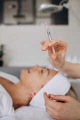 Obraz na płótnie Canvas Beautician doctor with botulinum toxin syringe making injection to to remove crow's feet. Cheek volume enhance mesotherapy. Anti-aging treatment and face lift in cosmetology clinic