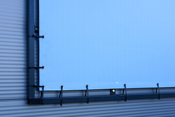 Fragment of the outdoor light blue advertising banner fastened to the black metal frame, mockup