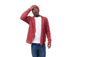 upset young american man in red cap and plaid shirt holding his head on white background with copy space