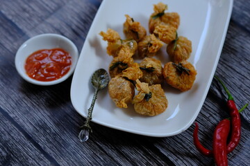 Ekkado is a food made from 3 main ingredients, namely quail eggs, shrimp, and tofu flowers/skin. Ekkado on white plate on wooden table. Tomato sauce next to plate. 