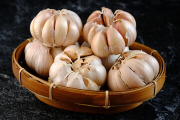a whole pile of garlic in a woven bamboo basket on the black marble. Garlic is commonly used as a food ingredient in the Mediterranean region, as well as a common spice in Asia, Africa, and Europe.