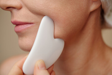 Closeup image of middle-aged woman using gua sha when massaging lower part of her face
