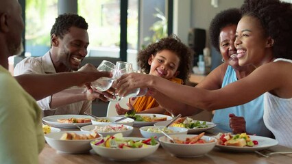 Multi-generation family sitting around table at home doing cheers with water glasses at meal - shot in slow motion - Powered by Adobe