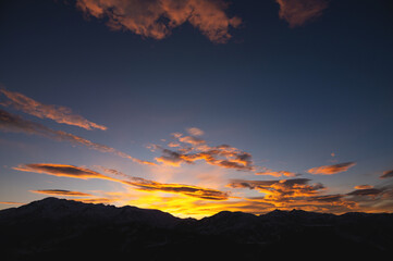 Colorful sunset over mountain hills. The black silhouette of the mountains is visible through the picturesque glow