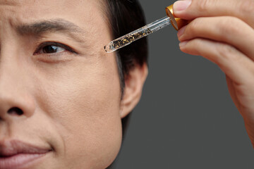 Closeup image of man applying essence to prevent eye wrinkles
