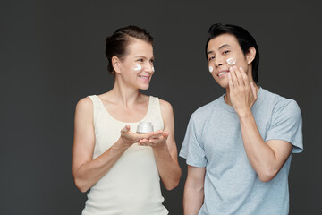 Happy man and woman applying rich nourishing cream on face