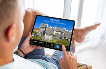 Man looking at real estate website on tablet computer, searching for a new house to buy