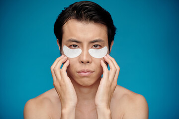 Serious man applying undereye patches to get rid of dark circles