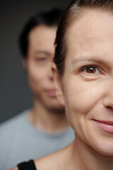 Half face of mature woman smiling at camera, man standing behind