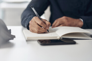 Setting deadlines for myself and my goals. an unrecognizable businessman sitting alone in his office and writing notes in a notebook.