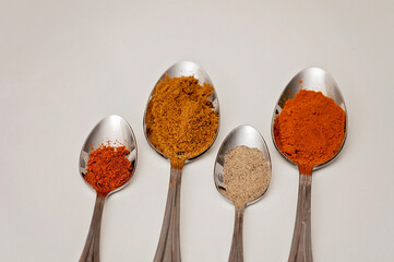 Four silver spoons with piles of spices on them on a white table. Middle Eastern and Asian grounded...