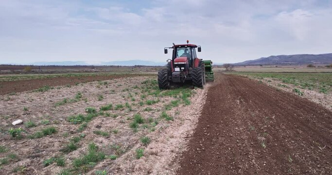 Spring agricultural field work, a tractor with a mounted seeder sow seeds in the ground on an field. aerial video