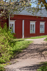 Old red wooden barn house in rural area with green yard, lawn or grass, trees and bushes. Traditional Scandinavian countryside building with many white framed windows on a warm and sunny summer day.