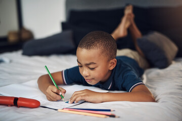My teacher said I should practise my alphabet at home. a young boy using colouring pencils while writing at home.