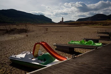 Tuinposter Boats are seen on scorched earth and earth clods on dry land caused by drought and lack of rain due to climate change. Concept of water shortage and climate crisis, cracked earth and dry soil. © davide bonaldo