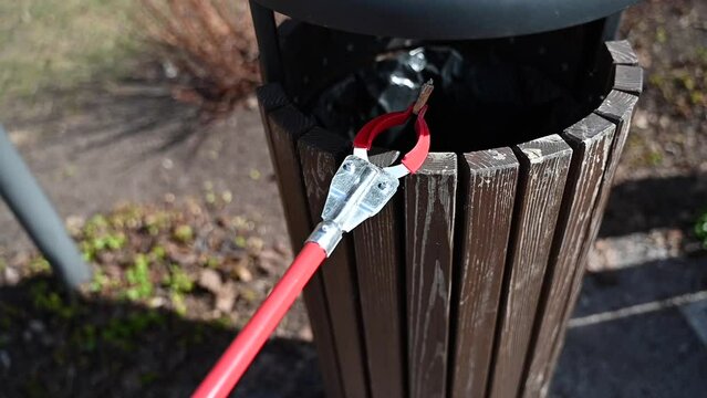 Person with Grabber Reacher Tool putting cigarette butts from ground into trash bin