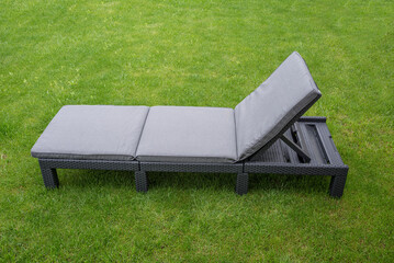 Plastic outdoor rattan bed with a cushion pad on a lawn