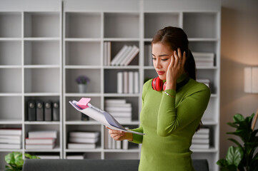 Focused and serious Asian businesswoman stands in her office reading documents