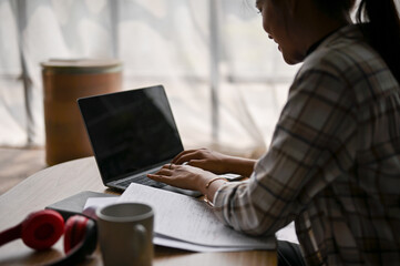 Close-up image of an Asian woman using her laptop at a coffee table in a living room.