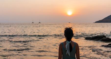 Rear view of beautiful young Asian female on a beach at sunset or sunrise. Summer, vacation and holiday concept. Copy space, closeup
