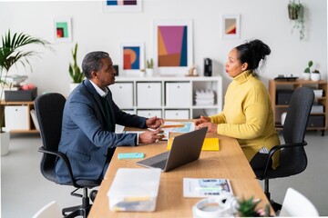 Side view of smiling Ethiopian woman and man in smart casual clothes talking while looking at each other in modern office