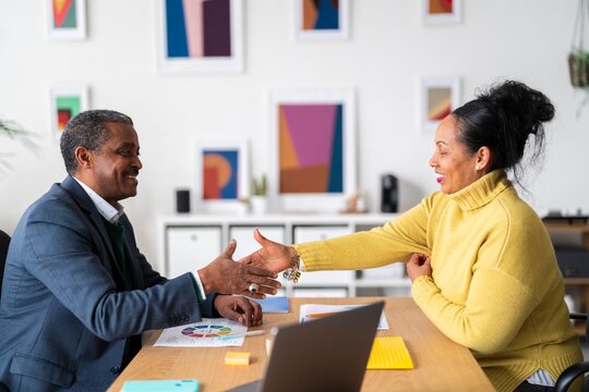 Side view of smiling Ethiopian woman and man in smart casual clothes shaking hands after successful discussion while looking at each other in modern office