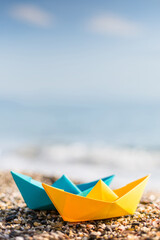 Blue and yellow paper boats on the pebble beach	
