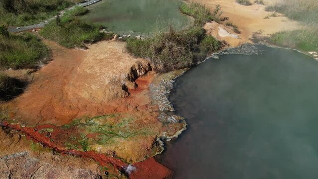 Steam from colorful mineral hot springs and mountain scenery of West Coast, New Zealand. Drone shot