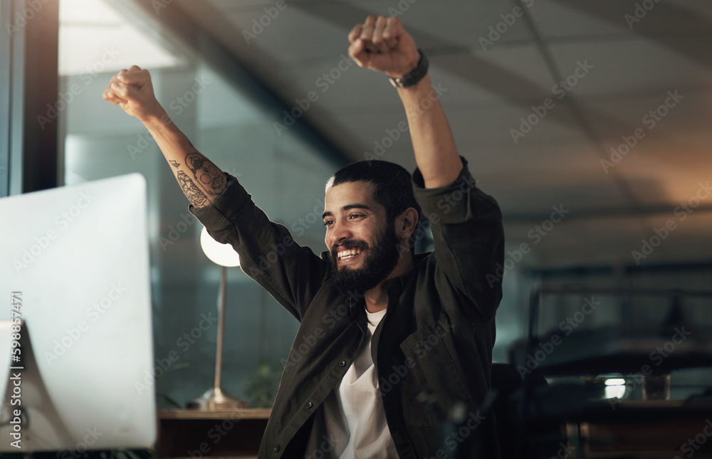 Poster Putting in the hours gets you that perfect score. a young businessman cheering while using a computer during a late night at work.