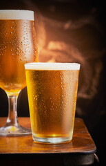 Two cold glasses of beer resting on a wooden table.