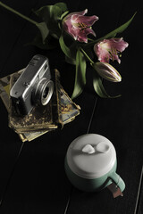 A simple still life with a vintage camera, some flowers and a cup of tea with a lid