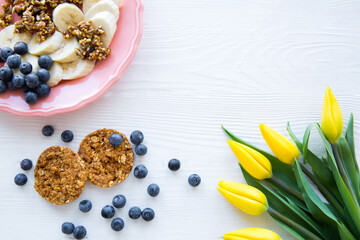 A plate of healthy breakfast, cookies, bananas and blueberry in white wooden background, top view. 