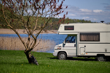 old school white camper parked on the grass by the lake. A vintage house on wheels in a sunny aura.