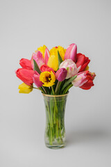Bouquet of colorful tulips in glass vase on white background. Vertical shot.