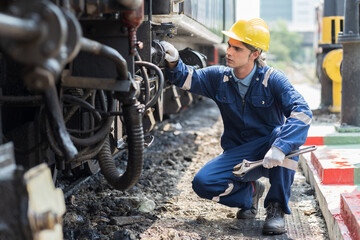 Male engineer worker maintenance locomotive engine, wearing safety uniform, helmet and gloves in locomotive garage. Male railway engineer repair railhead engine in garage