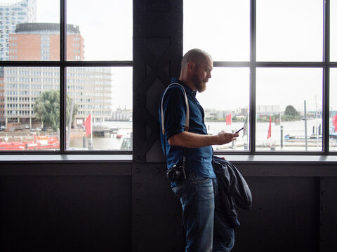 Man with camera looking at smart phone by window
