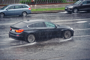 Car driving fast on wet road, driving through puddle during heavy rain. Car driving on flooded...