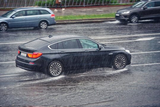 Car driving fast on wet road, driving through puddle during heavy rain. Car driving on flooded asphalt road. Dangerous driving conditions, wet road risk of aquaplaning. Slippery road, low visibility