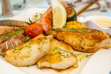 Grilled delicious fish fillets and shrimps with vegetables and lemon slices. Mediterranean diet.