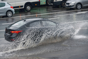 Car splashing water, driving through puddle at heavy rain. Car driving on flooded asphalt road at heavy rain, wet road. Dangerous driving conditions, risk of aquaplaning. MOTION BLUR.