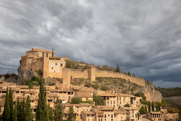 Fototapeta na wymiar Impressive panoramic view of the touristy medieval village of Alquezar situated on a hill surrounded by mountains with small brick houses and a large walled church at the top.
