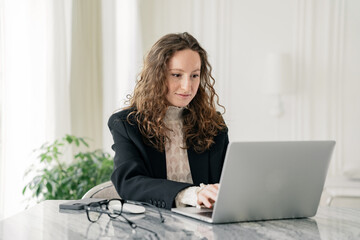 A business lady uses a laptop, a young woman in the office is sitting in stylish business clothes....