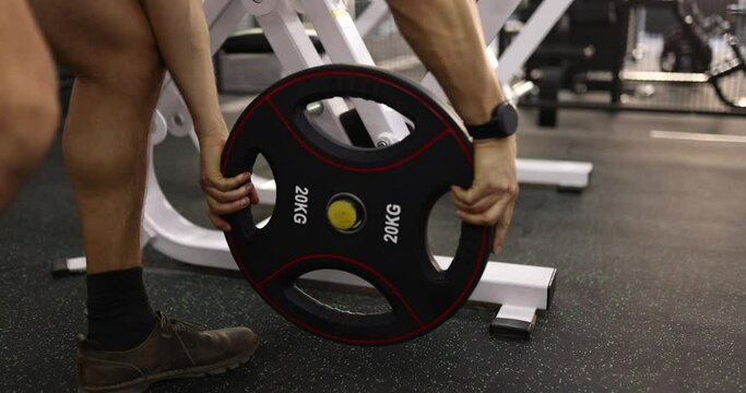 Athlete putting disc for barbell on rack in 20 kg gym closeup 4k movie slow motion. Power load on hands concept