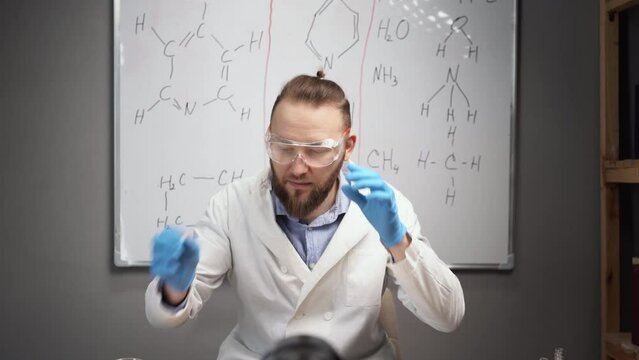 online tutor chemistry teacher records vlog in home video studio at home. A bearded man in a white coat sits on the background of a whiteboard. wears protective goggles