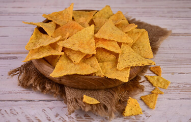 Corn chips in a wooden plate on a white wooden background.
